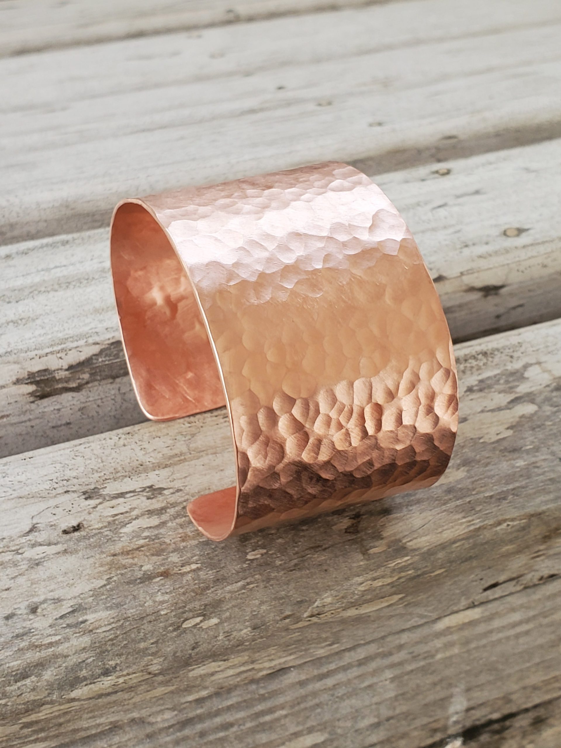 Wide hammered copper cuff bracelet shown on a wooden background from the side view