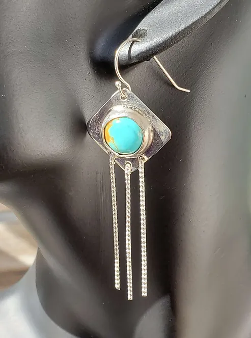 Round Turquoise Cabochon set in a diamond shaped sterling setting with three long textured silver dangle wires on french wire earrings shown on a mannequin.