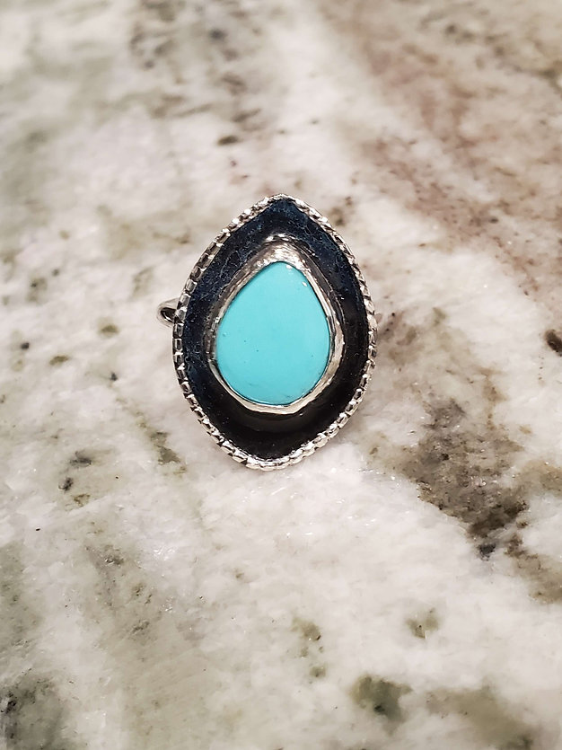 Teardrop Turquoise Cabochon set on an enameled sterling silver face and sterling band shown on granite.