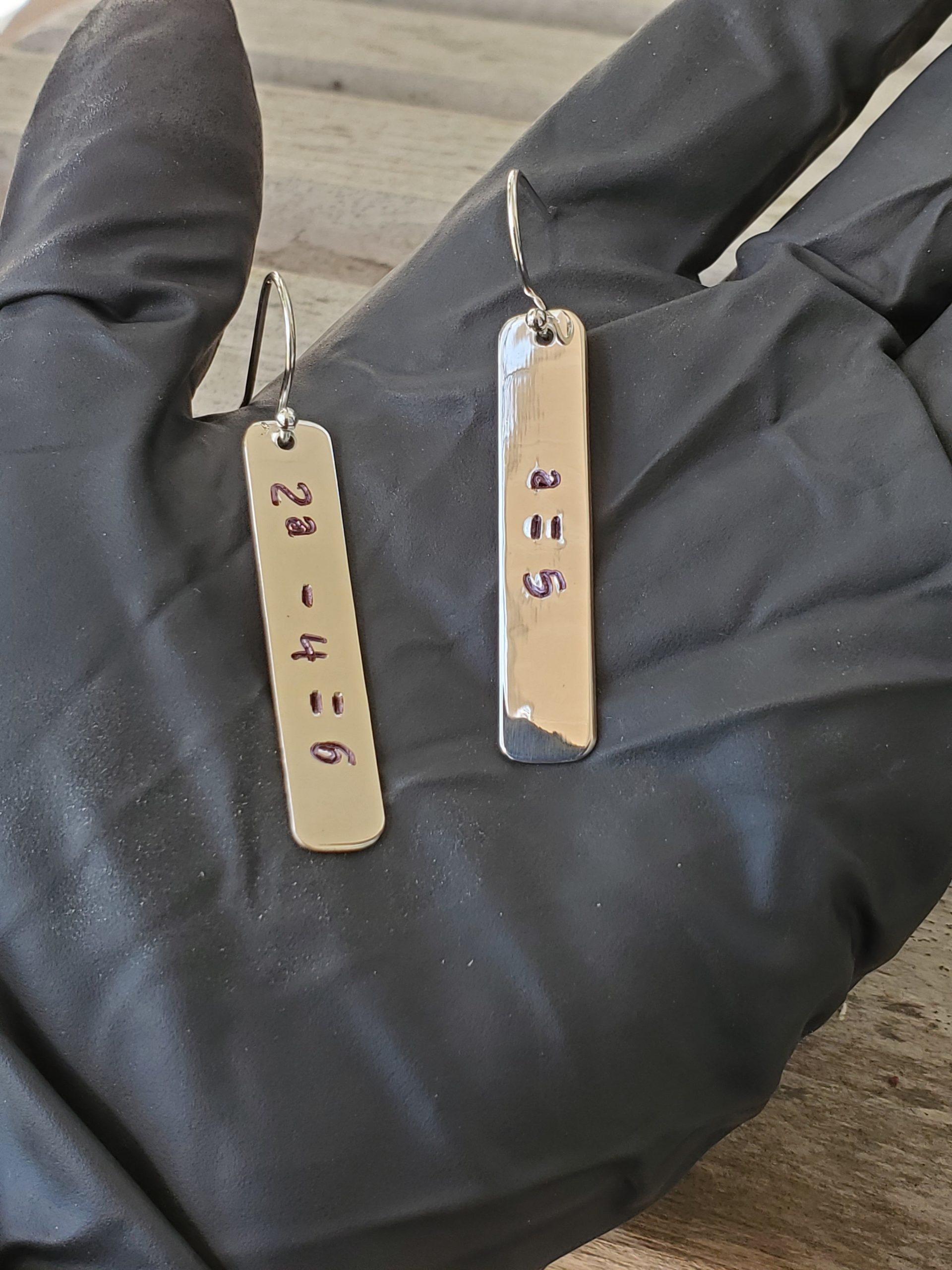 Stamped Algebra Equation Rectangle Sterling Silver Earrings showing 2a minus 4 equals 6 on one earring and a equals 5 on the other. Shown on model's hand.