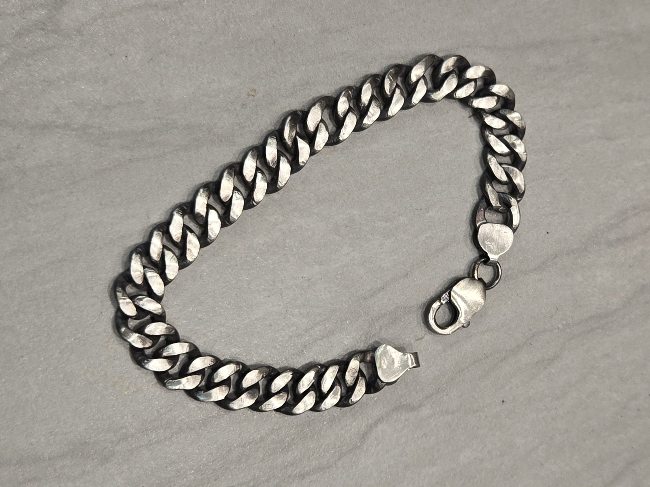 Cuban Link Sterling Silver Chain Bracelet with lobster clasp opened on a gray surface