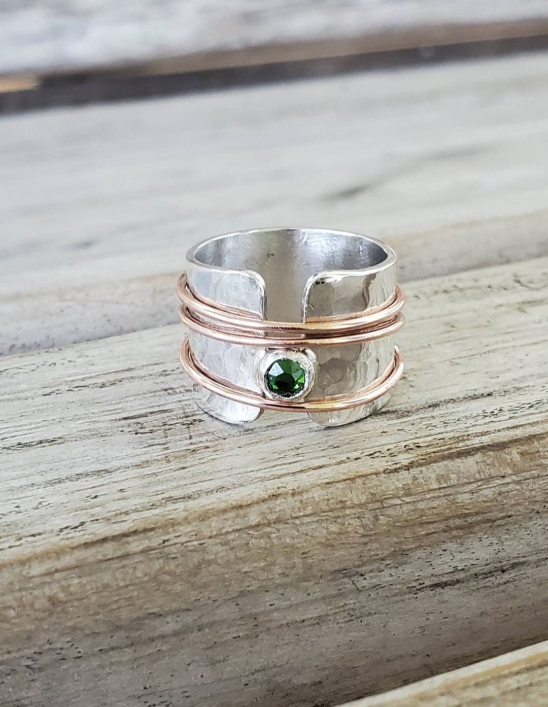 Personalized Hammered Sterling Silver Emerald Gemstone Copper Spinner Ring with 3 copper spinners on a wooden surface