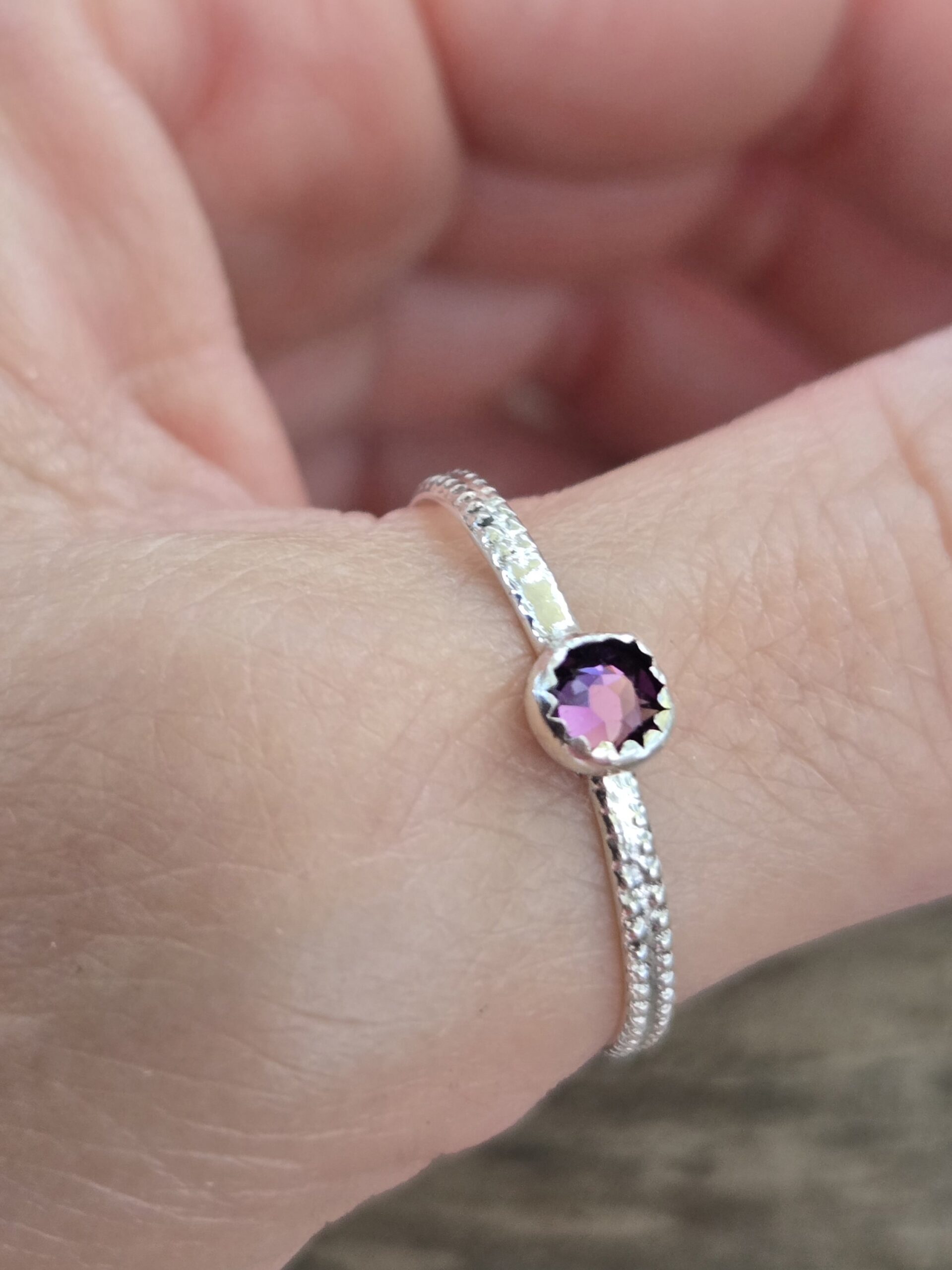 Slim Textured Sterling Silver Gemstone Stacking Ring shown on model's thumb with a round serrated bezel, small faceted crystal and textured ring shank