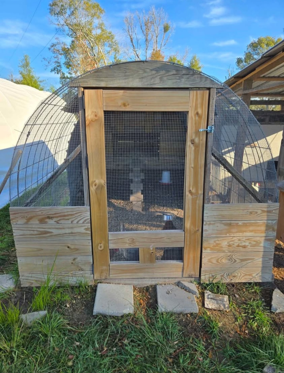 Front view of chicken coop covered in hardware cloth and sheet metal. Wood framed. The door is covered in hardware cloth and has a small latch.