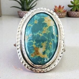 Oval Turquoise Cabochon set in a sterling bezel on a sterling silver ring shows the greenish blue and golds running throughout the stone.
