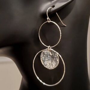 Long stacked sterling silver earrings with one hoop at the top and one hoop at the bottom with a hammered silver disc in it, shown on mannequin.