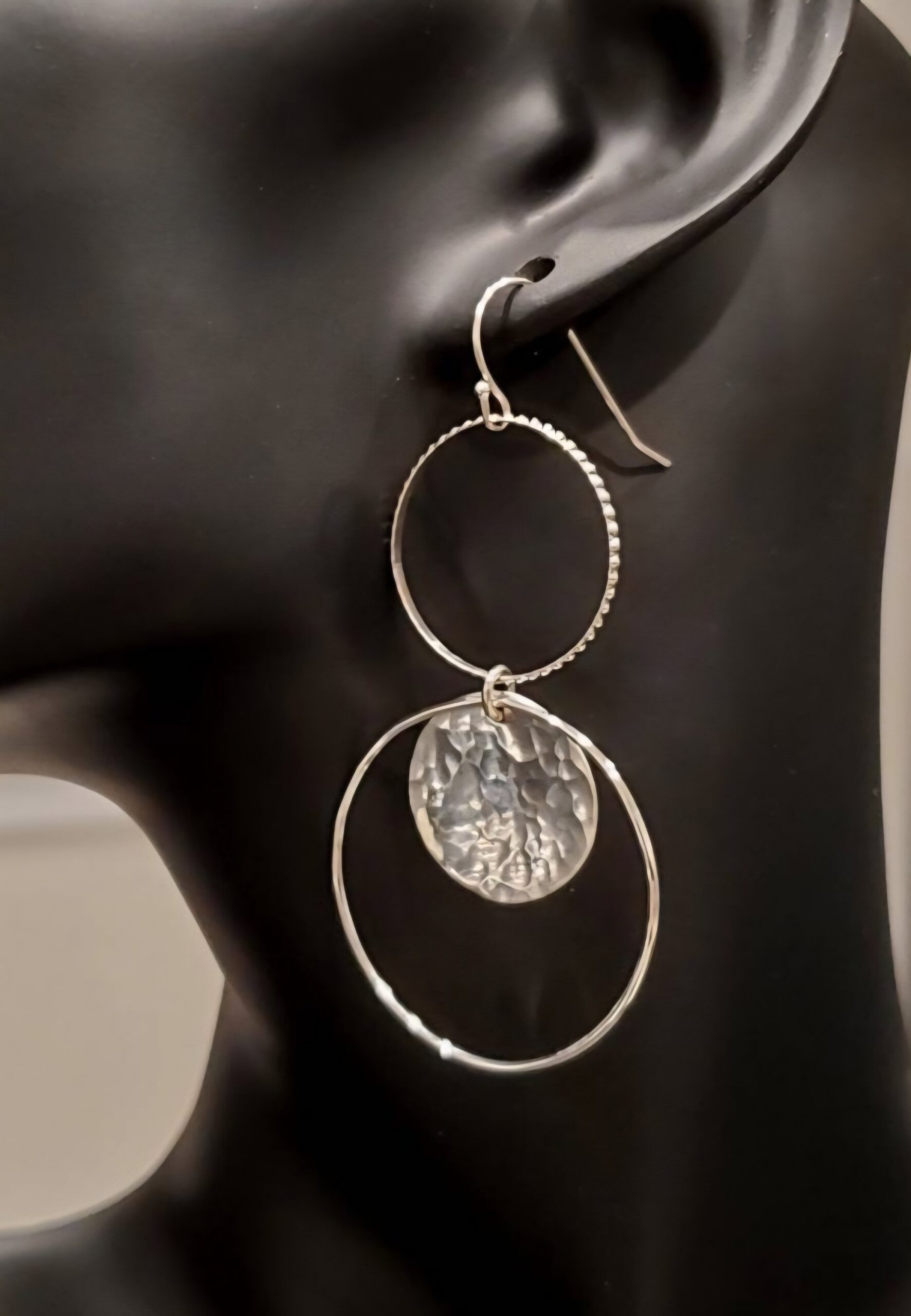 Long stacked sterling silver earrings with one hoop at the top and one hoop at the bottom with a hammered silver disc in it, shown on mannequin.
