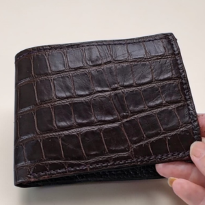 Dark brown alligator leather covers the bifold wallet. There's handstitching along the edges.