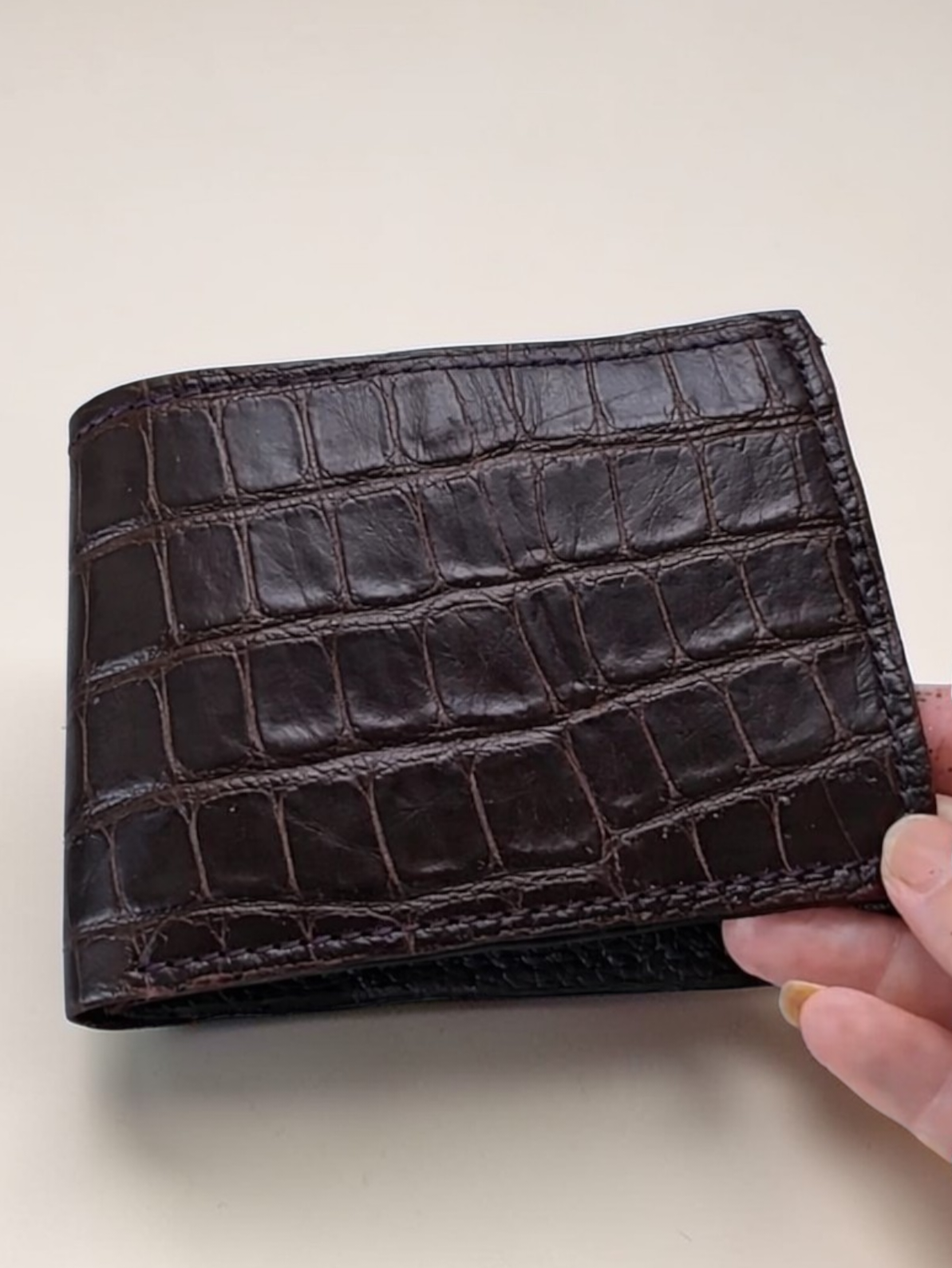 Dark brown alligator leather covers the bifold wallet. There's handstitching along the edges.