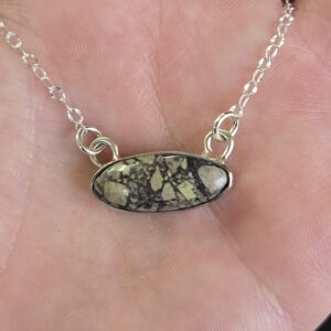 Maker holding oval cabochon pendant in her hand to show earthy tones and multiple shapes embedded in the stone face.