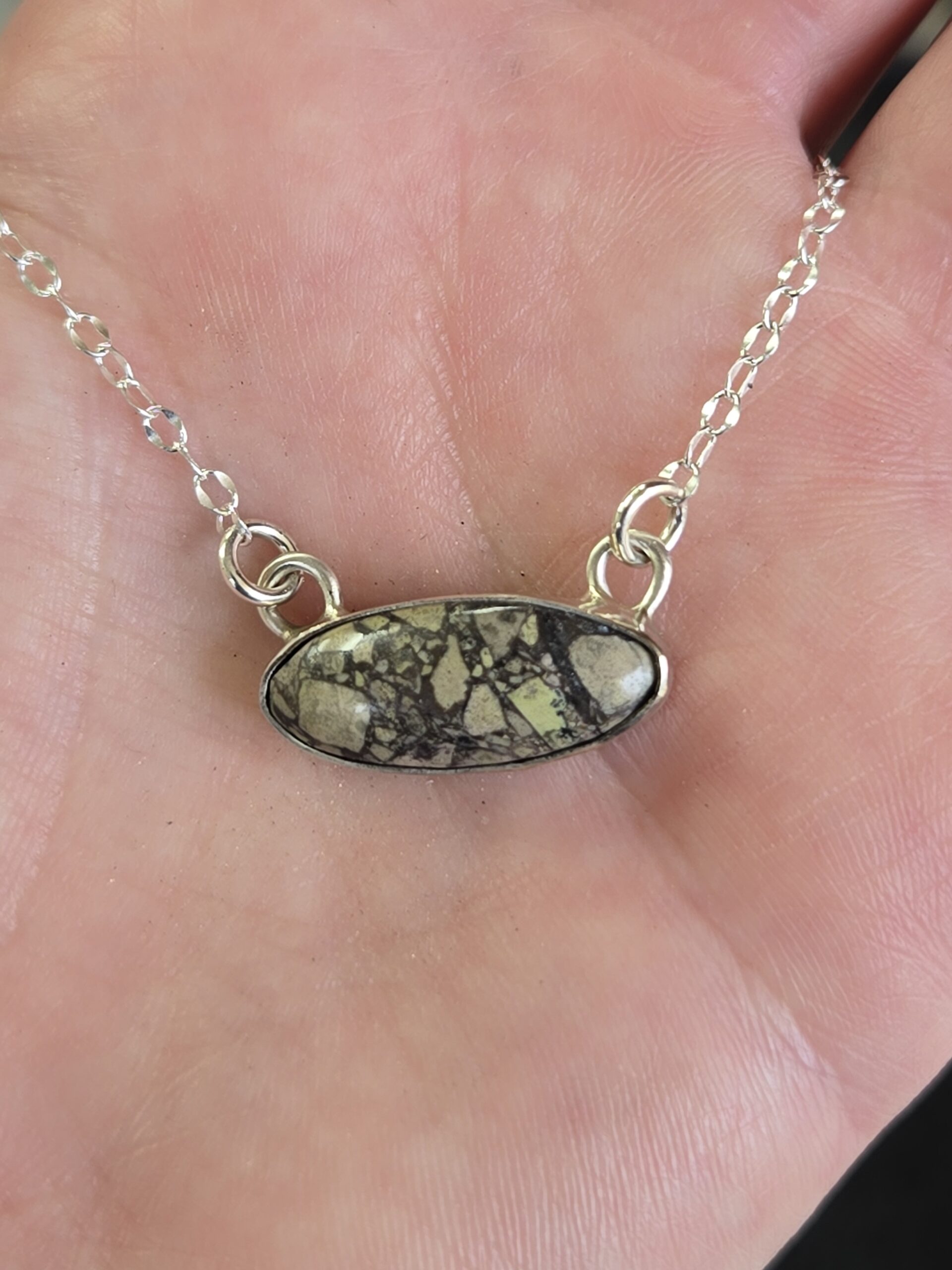 Maker holding oval cabochon pendant in her hand to show earthy tones and multiple shapes embedded in the stone face.