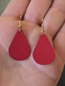 The maker holding her red Leather Teardrop Earrings.