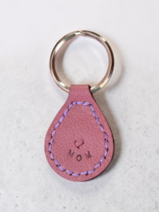 Light red Leather stitched in light purple and stamped with a heart and MOM on a stainless steel key ring.