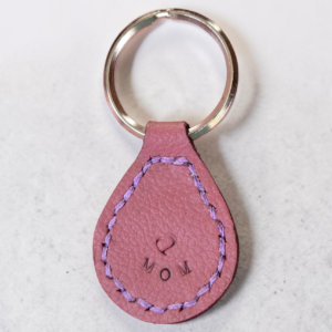 Light red Leather stitched in light purple and stamped with a heart and MOM on a stainless steel key ring.