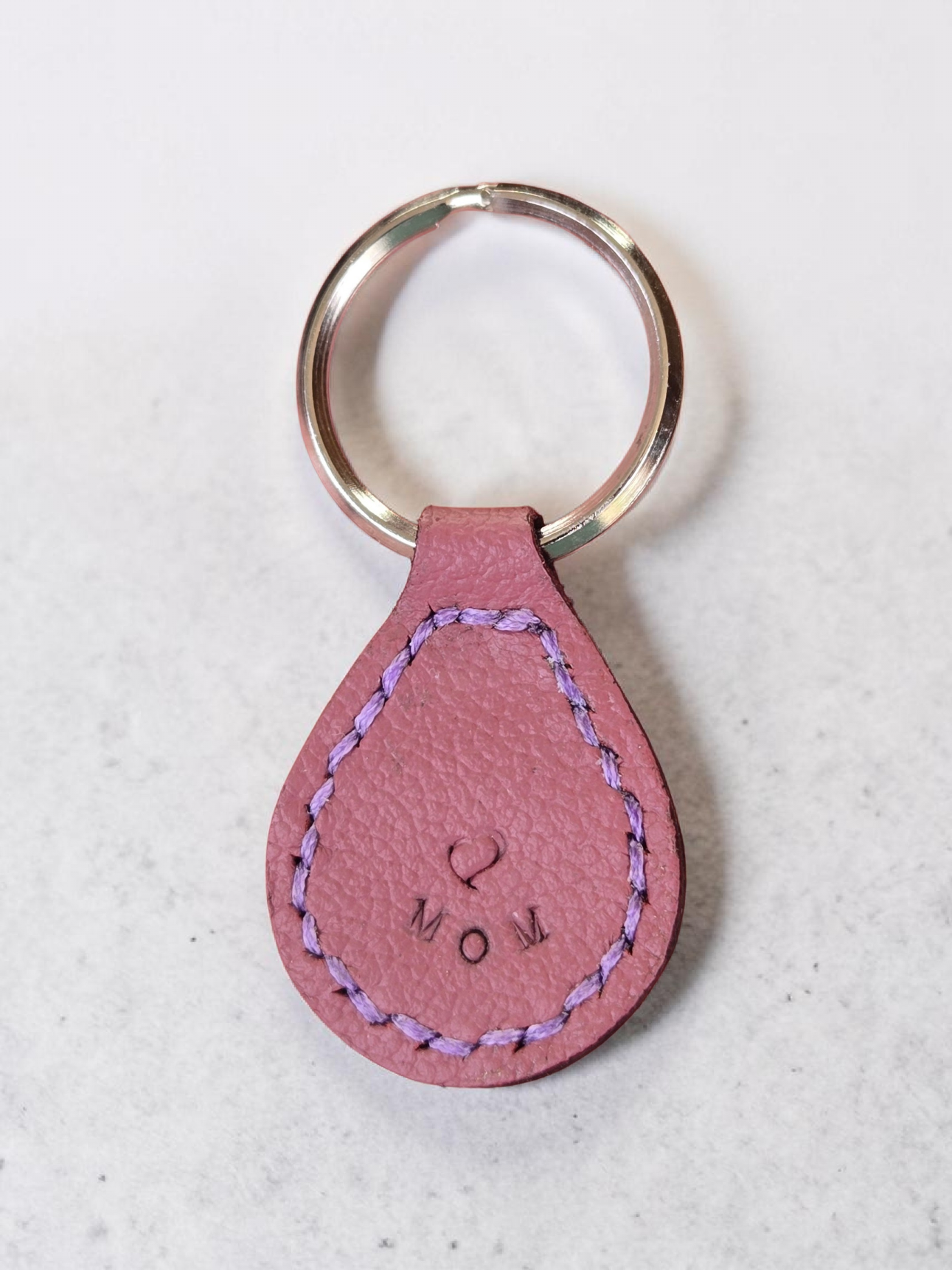 Light red Leather stitched in light purple and stamped with a heart and MOM on a stainless steel key ring.